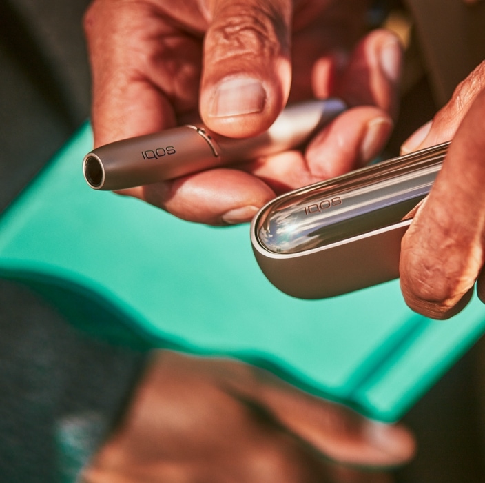 Brilliant gold IQOS 3 DUO with HEETS stick in hand and charger